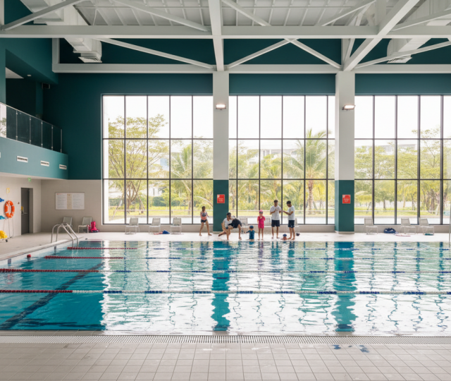 Modern Singapore indoor pool with turquoise water, families learning with instructors, tropical greenery view.