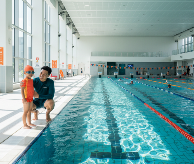 Child and coach by Olympic pool, bright, modern Singapore sports center.