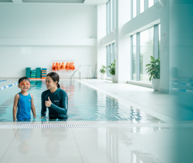 Child with instructor at bright, modern Singapore pool; teal and orange accents.
