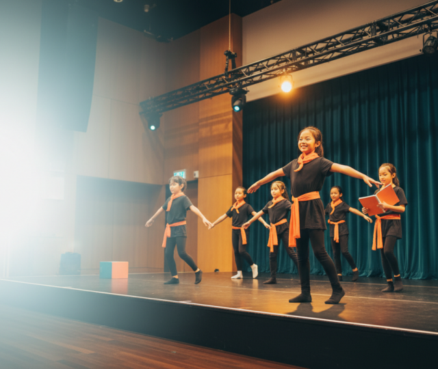 Diverse children perform on stage in modern Singapore studio, warmly lit, with mentor guidance.