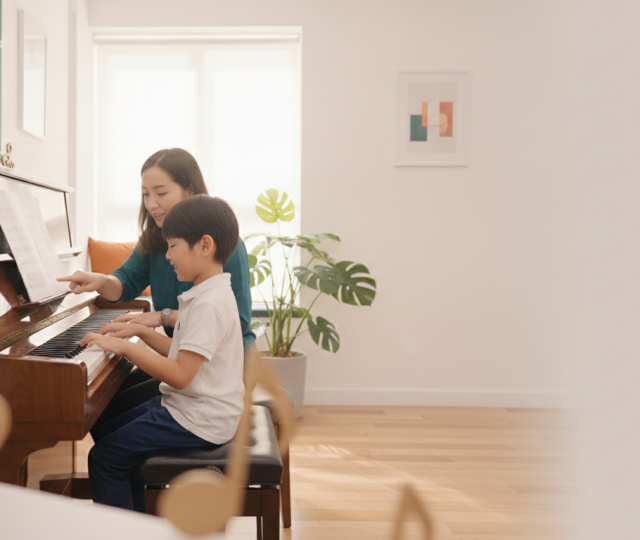 Young Asian child at piano in modern Singapore studio, with music teacher guiding.